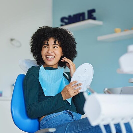 cosmetic dentistry women smiling in dentist chair holding mirror