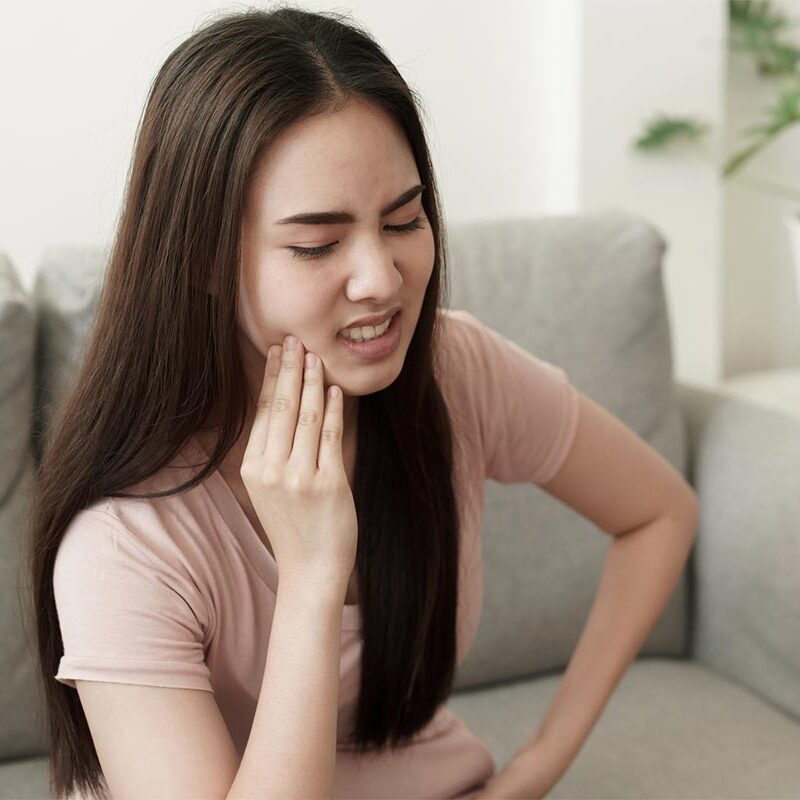 dental emergency young women sitting on couch holding sore mouth